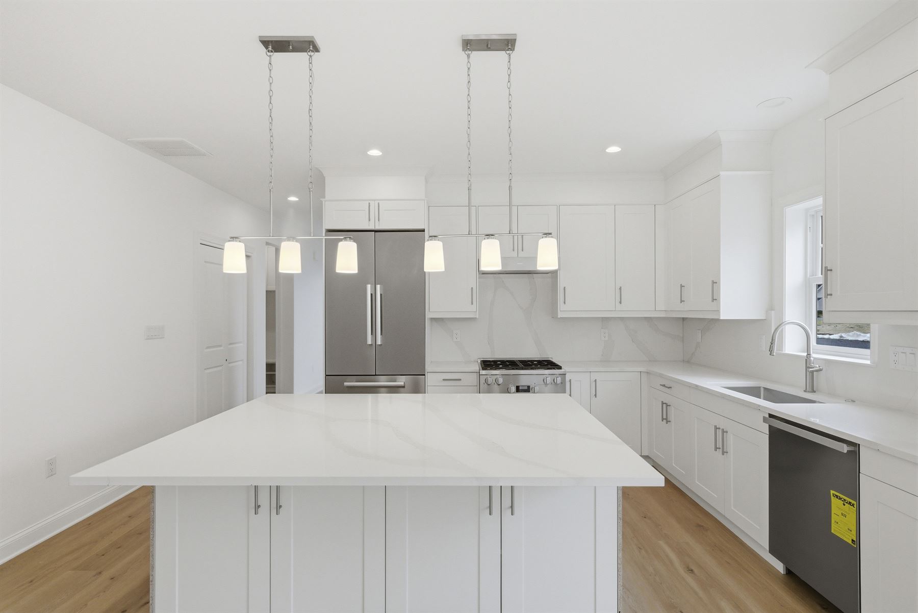 White kitchen with a quartz island, pendant lighting and stainless appliances